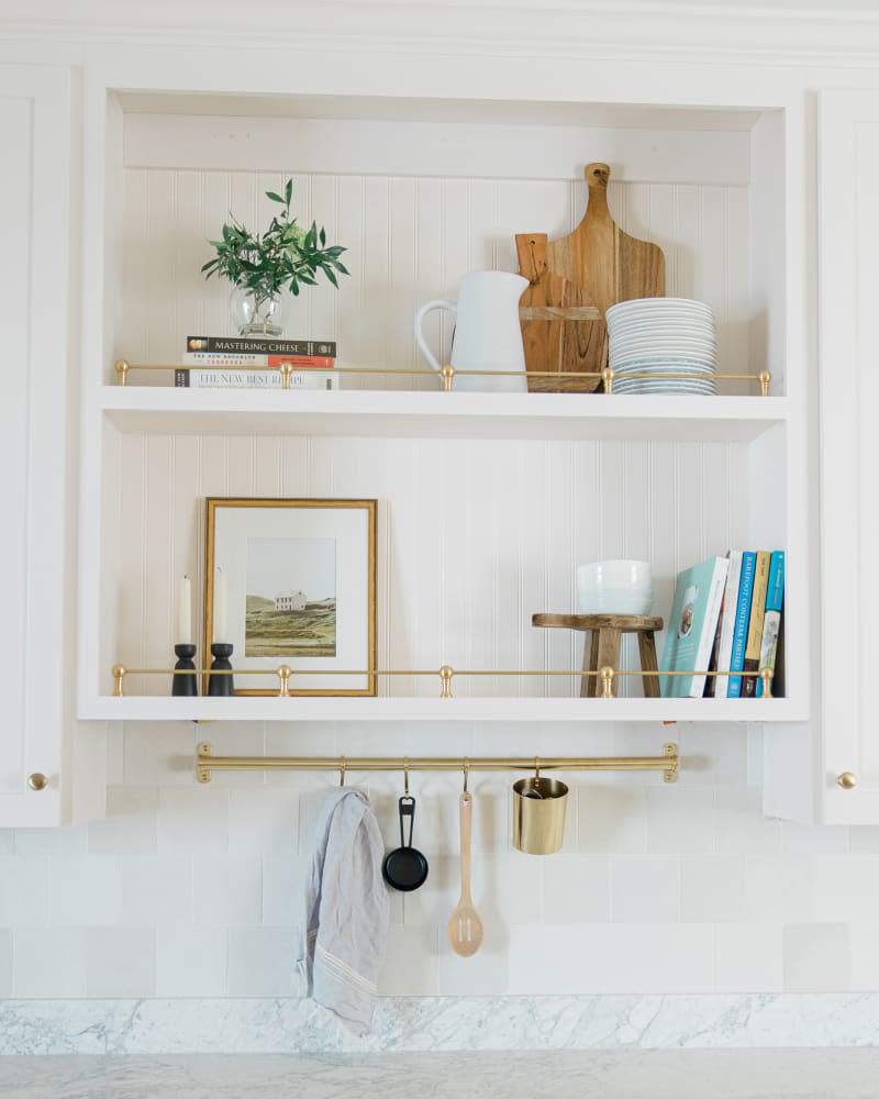 White kitchen open shelves with brass bars underneath for storing utensils