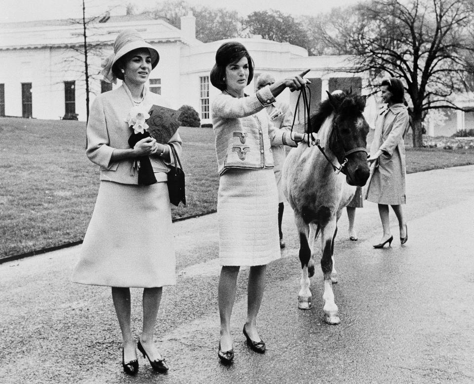 FILE - First lady Jacqueline Kennedy leads her daughter Caroline's pony, Macaroni, center, while giving gives a tour of the White House grounds to Empress Farah Pahlavi of Iran, on April 12, 1962. President Joe Biden and first lady Jill Biden have added a green-eyed tabby from Pennsylvania to the White House family. She's the first feline tenant since President George W. Bush’s controversially named cat India. With Presidents James K. Polk and Donald Trump among notable, no-pets exceptions, animals have a long history in the White House. (AP Photo/Pool, File)