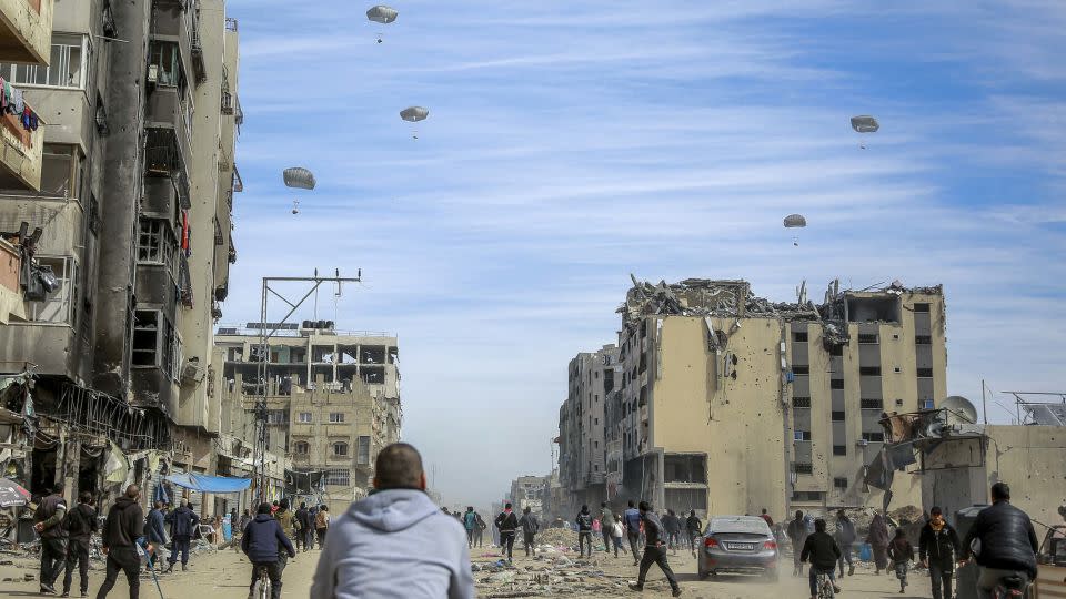 Palestinians run along a street as humanitarian aid is airdropped in Gaza City on March 1. - AFP/Getty Images