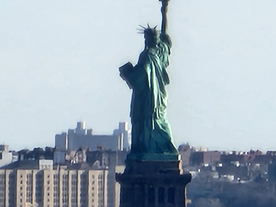 <p>A camera sample from the Galaxy S22 Ultra's Space Zoom feature showing a blurry image of the Statue of Libery with its back facing the camera and some buildings in front of it.</p>
