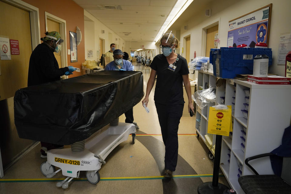 Chaplain Kristin Michealsen leaves a COVID-19 unit after talking to a family member of a deceased patient as transporters Noe Meza, left, and Miguel Lopez wheel a gurney carrying a body of a COVID-19 victim at Providence Holy Cross Medical Center in the Mission Hills section of Los Angeles on Saturday, Jan. 9, 2021. (AP Photo/Jae C. Hong)