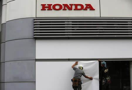 Workers stand under the logo of Honda Motor Co. outside the company's headquarters in Tokyo October 30, 2013. REUTERS/Issei Kato