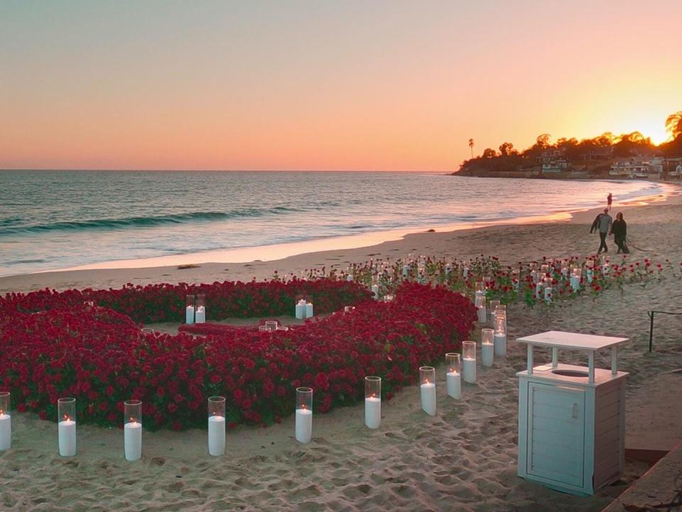 the site of travis barker's proposal to kourtney kardashian, a ring of roses surrounded by candles on a beach