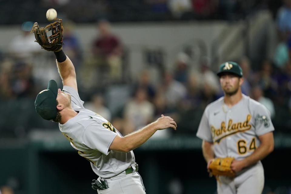 Oakland Athletics third baseman Sheldon Neuse reaches up to catch a popup by Texas Rangers' Leody Taveras, as starting pitcher Ken Waldichuk (64) watches during the fifth inning of a baseball game in Arlington, Texas, Tuesday, Sept. 13, 2022. (AP Photo/Tony Gutierrez)