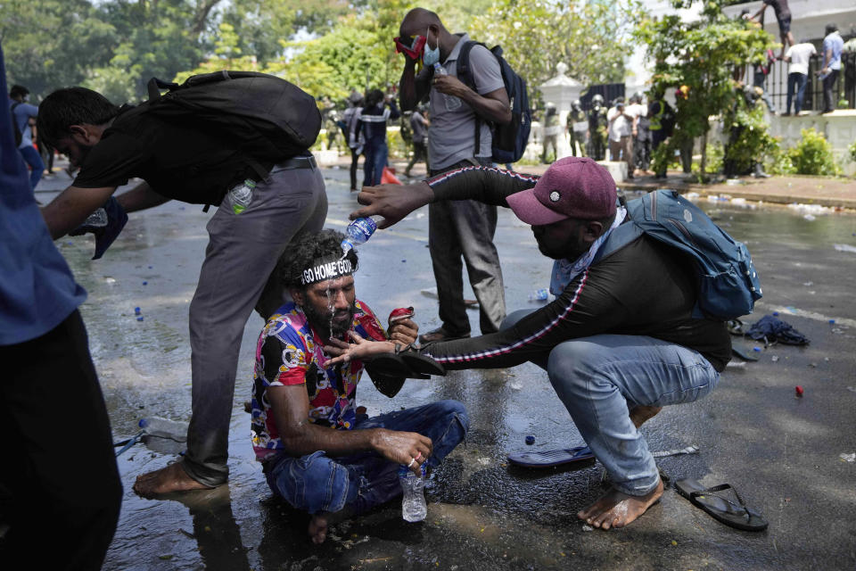 A protester helps another after police fired teargas to disperse them before they stormed Sri Lankan Prime Minister Ranil Wickremesinghe's office, demanding he resign after president Gotabaya Rajapaksa fled the country amid economic crisis in Colombo, Sri Lanka, Wednesday, July 13, 2022. Sri Lanka’s president fled the country without stepping down Wednesday, plunging a country already reeling from economic chaos into more political turmoil. Protesters demanding a change in leadership then trained their ire on the prime minister and stormed his office. (AP Photo/Eranga Jayawardena)