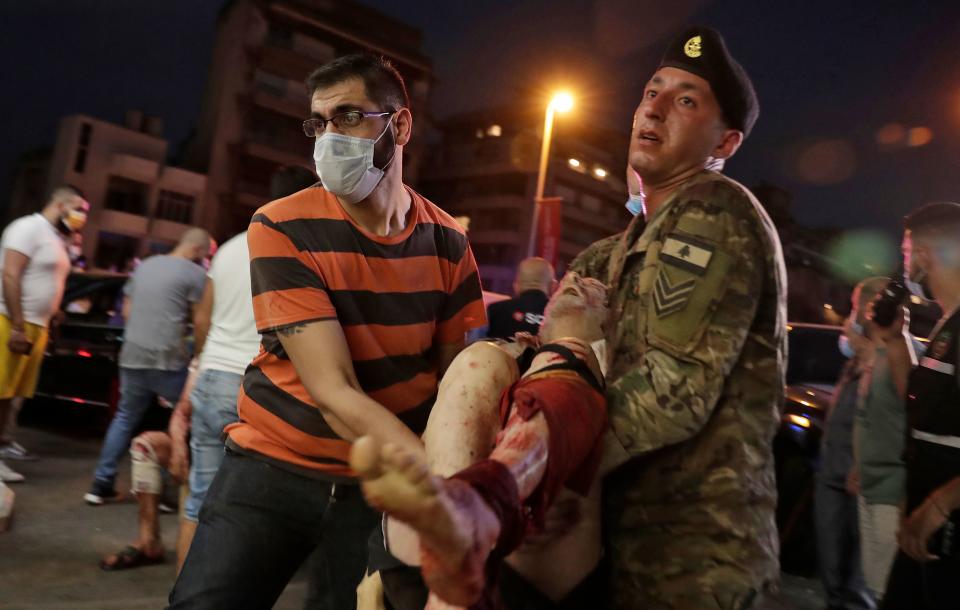 A Lebanese army soldier and a man carry away an injured man at a hospital in the aftermath of an explosion at the port of Lebanon's capital Beirut on August 4, 2020. - Two huge explosion rocked the Lebanese capital Beirut, wounding dozens of people, shaking buildings and sending huge plumes of smoke billowing into the sky. Lebanese media carried images of people trapped under rubble, some bloodied, after the massive explosions, the cause of which was not immediately known. (Photo by IBRAHIM AMRO / AFP) (Photo by IBRAHIM AMRO/AFP via Getty Images)