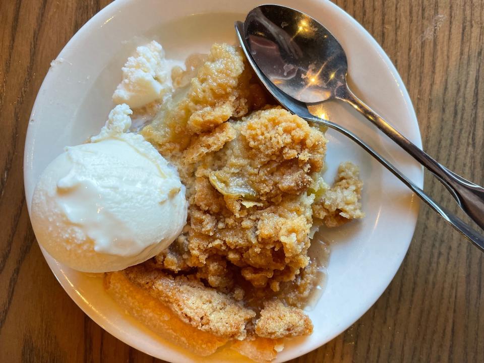 Apple-streusel pie with a scoop of vanilla ice cream and two spoons on a plate