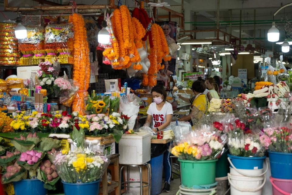 Vibrant orange garlands of marigolds hang above women preparing flowers at Samyan Market in Bangkok.