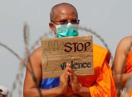 A Buddhist monk prays and holds a placard behind a wire barricade at Dhammakaya temple, in Pathum Thani province, Thailand February 23, 2017. REUTERS/Chaiwat Subprasom