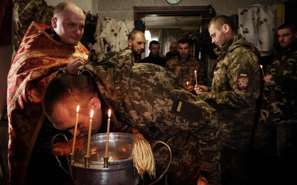 Mykola Berezyk (L), 28-year-old, chaplain to the Ukrainian Armys 95th Air Assault Brigade, also known as "Father Mykola, conducts a prayer for Ukrainian servicemen who returned from the frontline, as a serviceman kisses a cross in the Donetsk region on February 22, 2023, amid the Russian invasion of Ukraine. - YASUYOSHI CHIBA