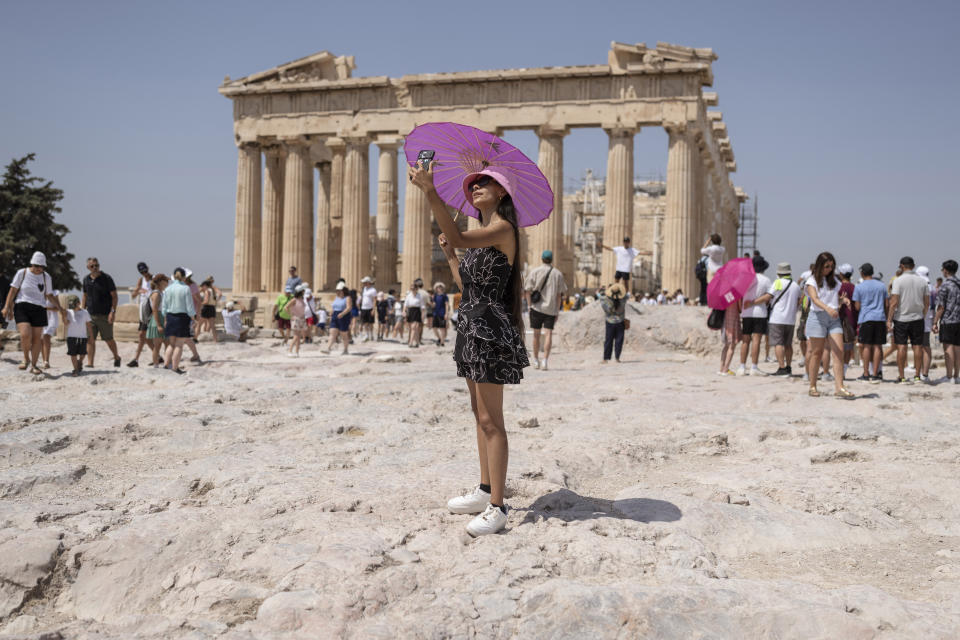 FILE - A woman takes a selfie in front of Parthenon temple atop of the ancient Acropolis hill during a heat wave in Athens, Greece, July 21, 2023. From April 1, 2024, Greece is planning to offer exclusive, guided tours of the Acropolis, its most powerful tourist magnet, to handfuls of well-heeled visitors outside normal opening hours. It will cost 5,000 euros ($5,500) for a group of up to five people. (AP Photo/Petros Giannakouris, File)