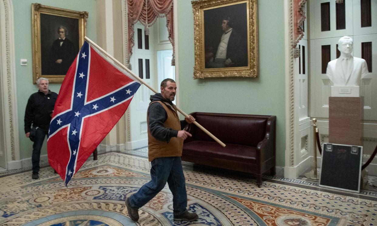 <span>A Trump supporter carries a Confederate flag through the US Capitol on 6 January 2021. He was released one year into his three-year term.</span><span>Photograph: Saul Loeb/AFP/Getty Images</span>