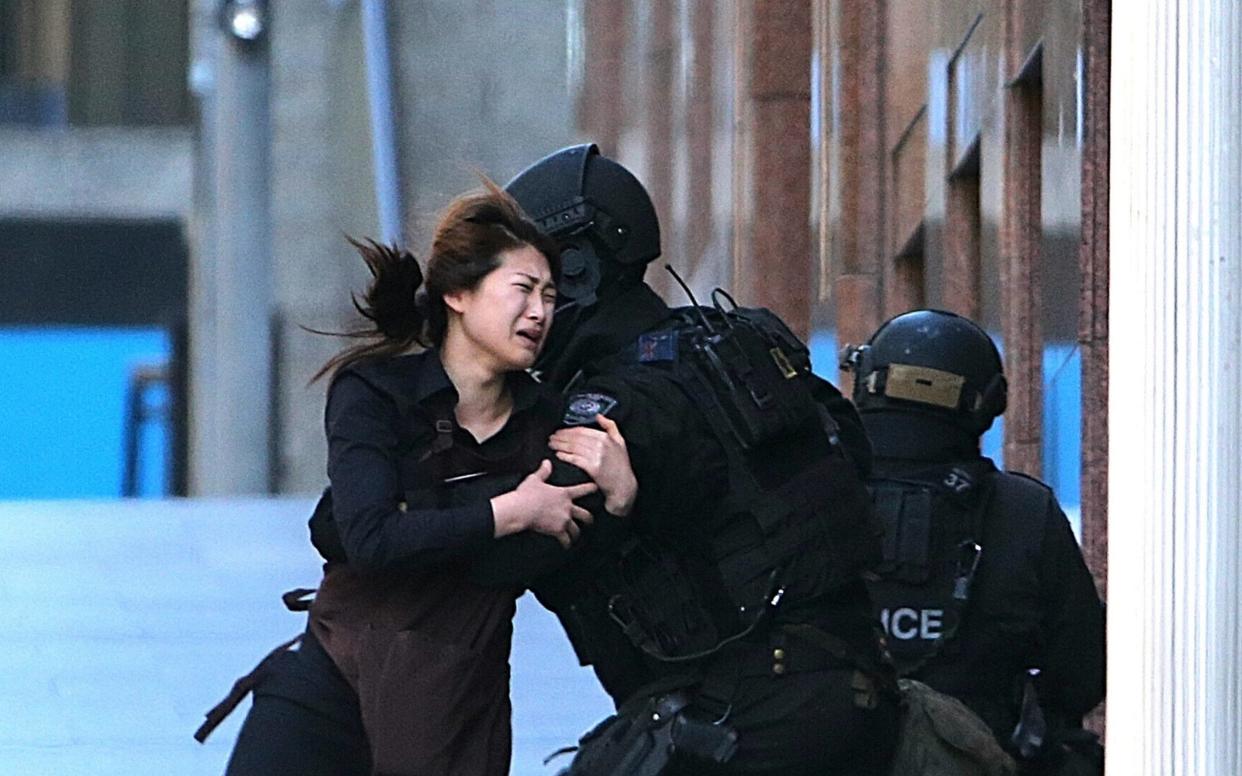 A hostage runs to armed tactical response police officers for safety after she escaped from a cafe under siege at Martin Place - AP