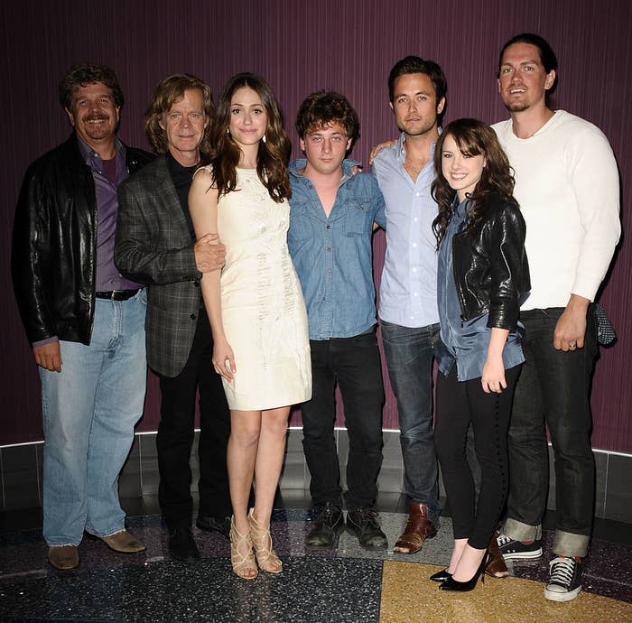 Seven cast members posing; one in a leather jacket, one in a white dress, and others in casual attire