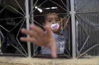 A girl reaches out from a window of her home built on squatted land that is occupied by hundreds of poor families in Rio de Janeiro, Brazil, Monday, June 20, 2022. (AP Photo/Silvia Izquierdo)