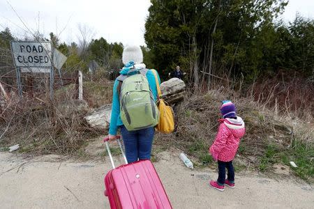 A mother and child are confronted by a Royal Canadian Mounted Police (RCMP) officer as they approach the U.S.-Canada border on Roxham Road in Champlain, New York, U.S., April 24, 2017. REUTERS/Christinne Muschi