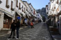 Two girls stand outside a shop as a municipality worker cleans a road in Gjirokastra town, southern Albania, Friday, Feb. 5, 2021. Tourism had been flourishing in the UNESCO-protected city of Gjirokastra but the coronavirus pandemic brought an abrupt halt to that, with the prospects still bleak in 2021, and now residents are calling for government help to keep their businesses afloat.(AP Photo/Hektor Pustina)