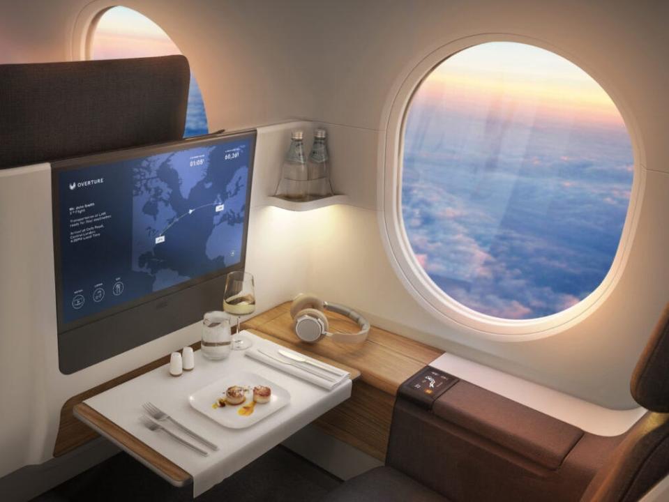 Example of a business class interior on an Overture with flatscreen TV, a tray table with food, and a giant window.