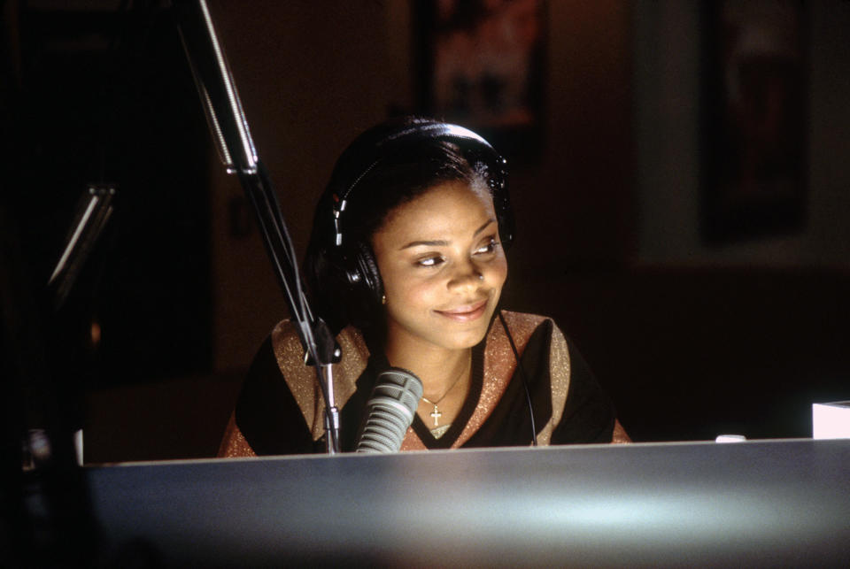 Person smiling at microphone, wearing headphones, in a radio studio setup
