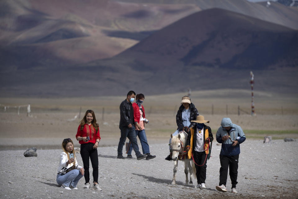 Un grupo de turistas camina junto a un lago y monta un burro en Namtso, al oeste de la Región Autónoma del Tíbet, el 2 de junio del 2021. El turismo chino es uno de varios factores que conspiran contra la supervivencia de las costumbres y creencias del Tíbet. (AP Photo/Mark Schiefelbein)