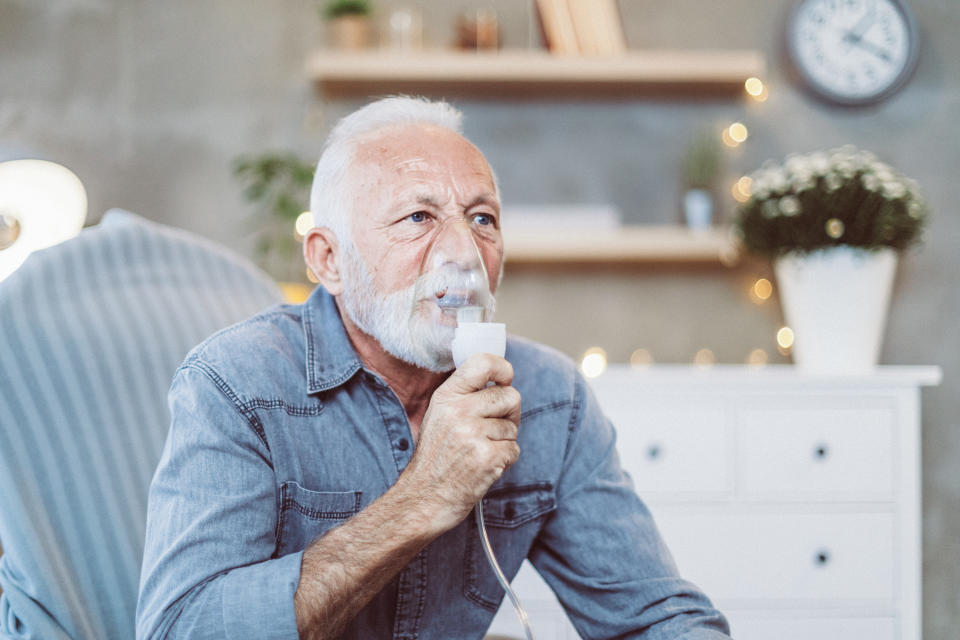 Portrait of senior sick man with grey hair at home inhaling  in isolation during the human pandemic. He inhales steam to treat a blocked nose during the day as alternative therapy or traditional cure. Rhinitis treatment at home by inhalation. Covid-19 virus