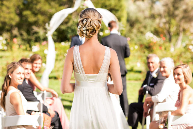 Rear view of young bride walking down the aisle while guests look at her. 
