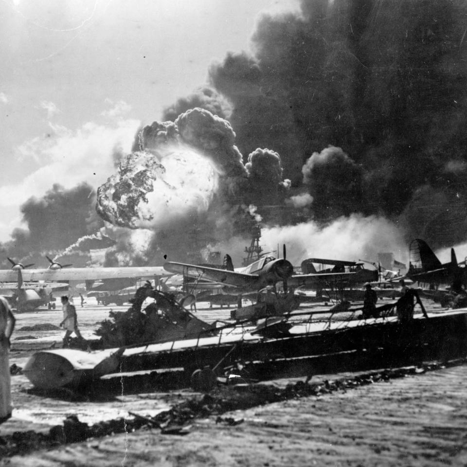 Historical photo of Pearl Harbor attack showing smoke, damaged airplanes, and people