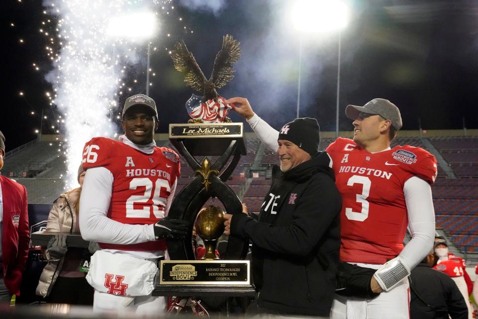Houston head coach Dana Holgorsen, center, looks on as he and defensive back Art Green (26) and quarterback Clayton Tune (3) hoist the Independence Bowl championship trophy following their win over Louisiana-Lafayette in an NCAA college football game Friday, Dec. 23, 2022, in Shreveport, La.