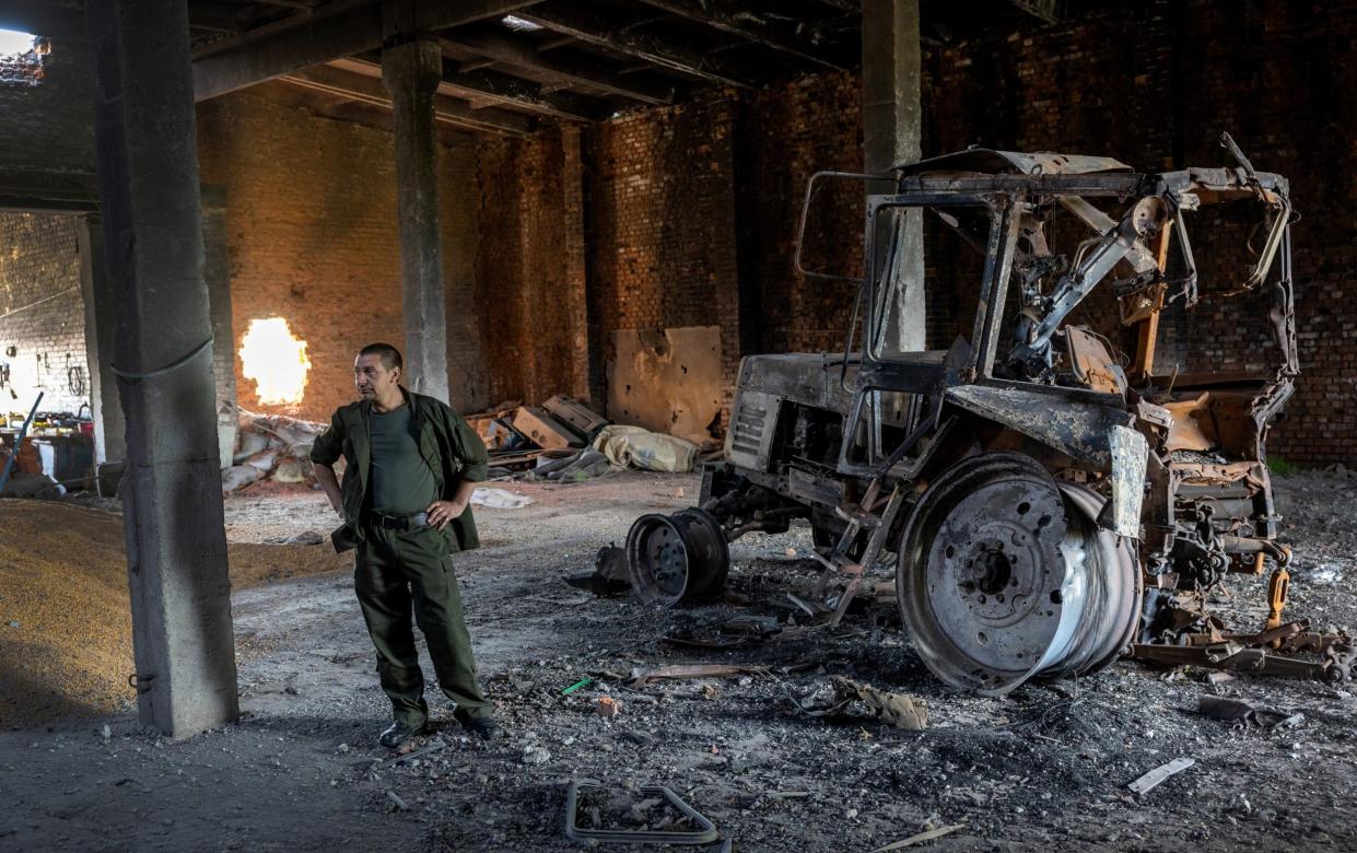 Ukrainian farm worker Misha stands near a tractor destroyed by a Russian tank shell - John Moore/Getty Images