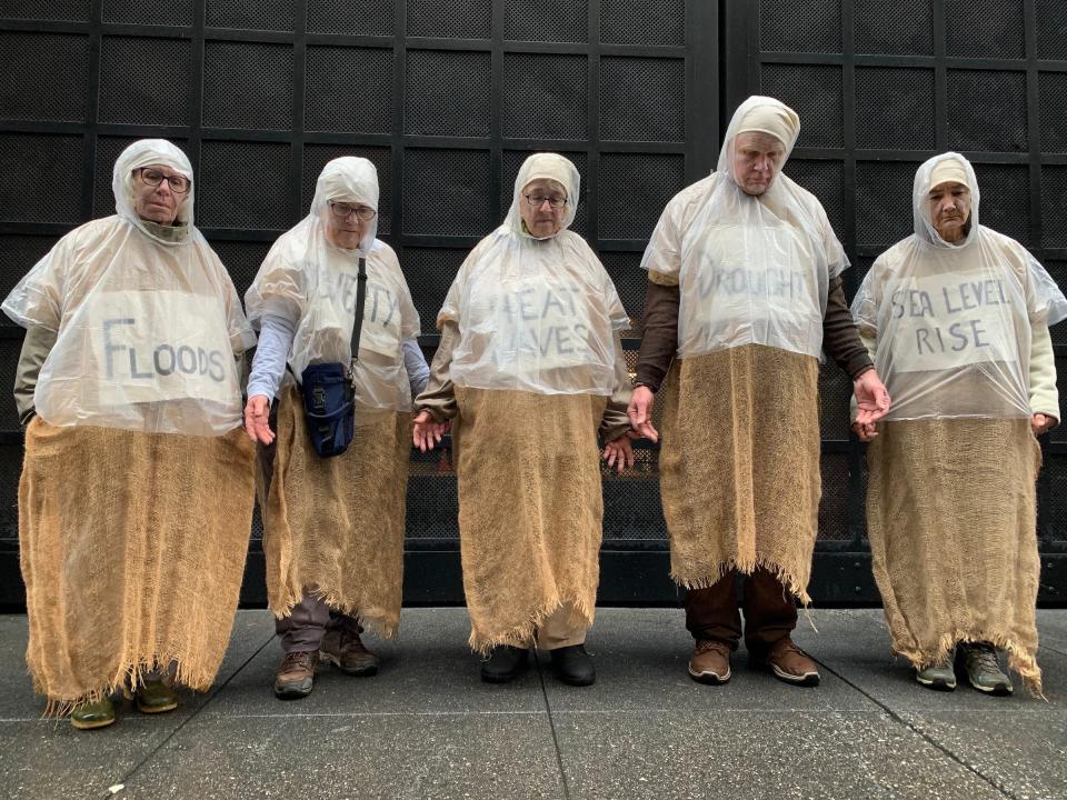five people in burlap sacks medieval costume wearing signs reading floods heat waves drought sea level rise