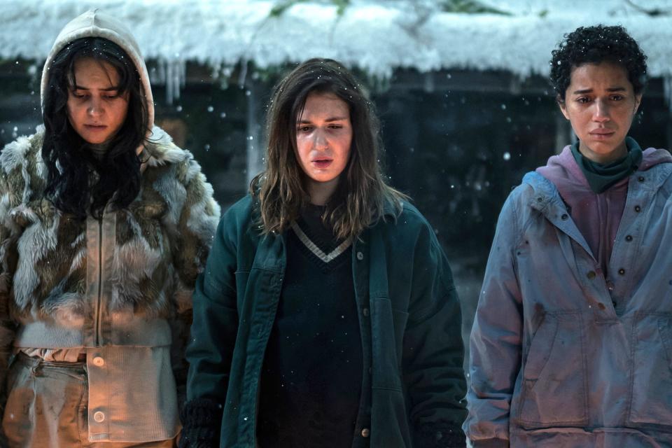 Teenage Lottie, Shauna, and Taissa stand bundled up outside in the snow, watching a fire in this still from season two, episode two of "Yellowjackets."
