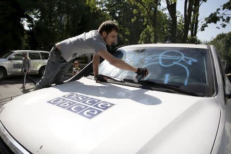 A demonstrator sprays graffiti on a truck of the Organisation for Security and Co-operation in Europe (OSCE) during a protest to demand what protesters say is true information from the OSCE about the shelling in Donetsk, Ukraine, July 23, 2015. REUTERS/Alexander Ermochenko