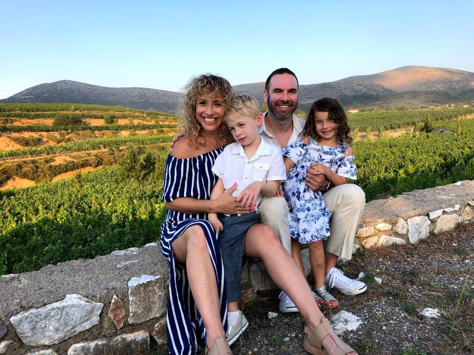 A family of 4 posing in front of a vineyard.