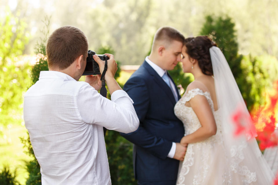 Wedding photographer with camera takes pictures of the beautiful bride and groom outdoors