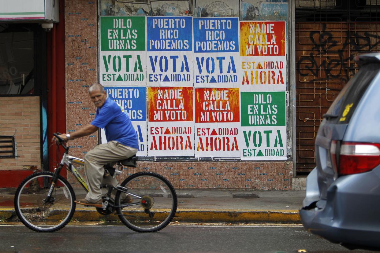 A man rides his bicycle in front of a wall covered with campaign posters promoting Puerto Rico's statehood in San Juan, on June 9, 2017.