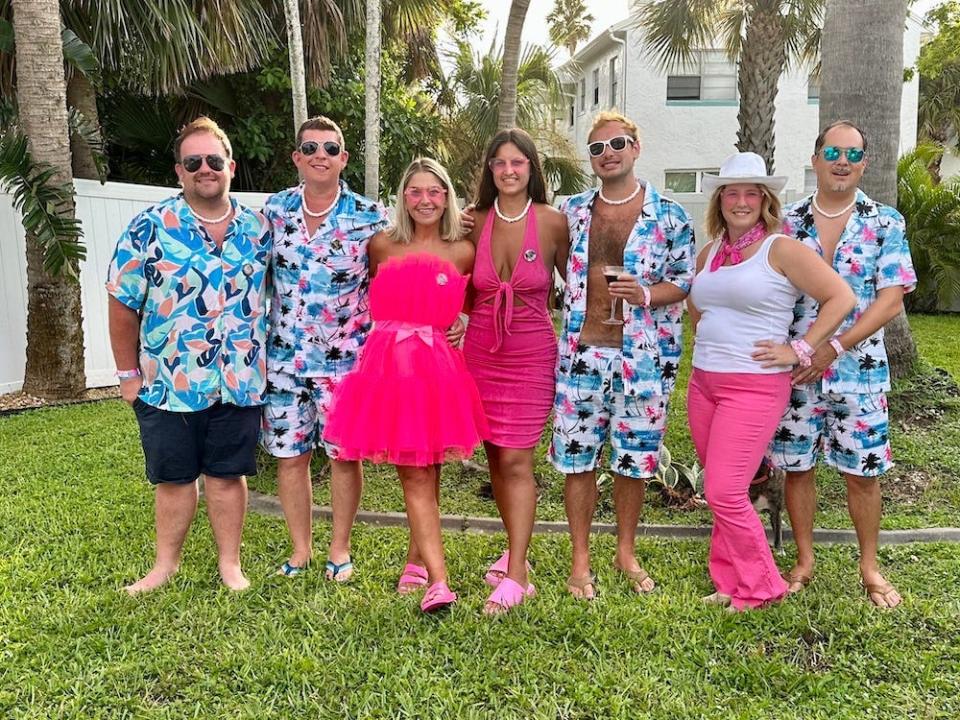 Photo of Terri Peters and her friends standing in a line with their arms on each other's shoulders. The women wear pink outfits and pink sunglasses. The men all wear colorful Hawaiian shirts and shorts. Behind them are palm trees.