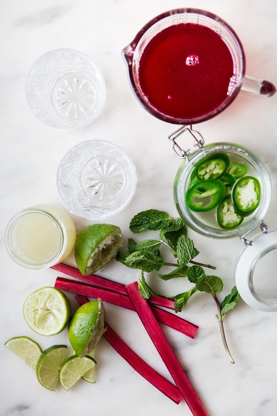 Assorted ingredients for a cocktail including lime, mint, jalapeno, and rhubarb on a marble surface