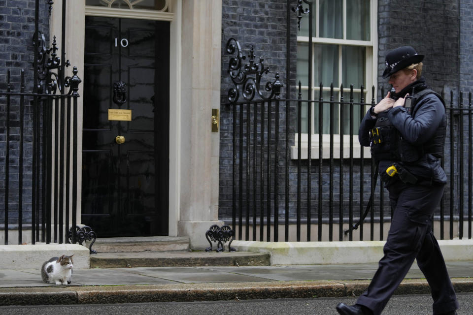 FILE - A police officer walks past 10 Downing Street while Larry the Cat, Britain's Chief Mouser to the Cabinet Office, sits on the pavement in London, Jan. 11, 2022. Some Conservative lawmakers in Britain are talking about ousting their leader, Prime Minister Boris Johnson, over allegations that he and his staff held lockdown-breaching parties during the coronavirus pandemic. The party has a complex process for changing leaders that starts by lawmakers writing letters to demand a no-confidence vote. (AP Photo/Frank Augstein, File)