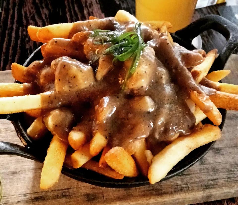fries covered in gravy in metal bowl on cutting board