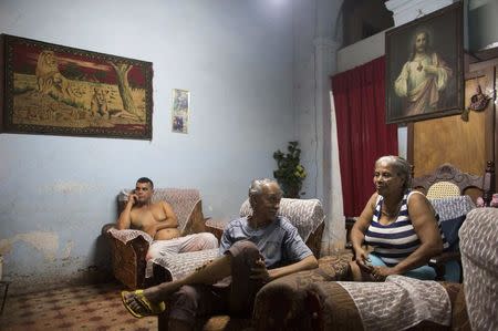 Andre Tamayo, 64, (C) talks to his wife Miriam Gonzalez, 67, (R) while they wait for clients in the living room of their home where they sell coffee through the window in Havana January 9, 2015. REUTERS/Alexandre Meneghini