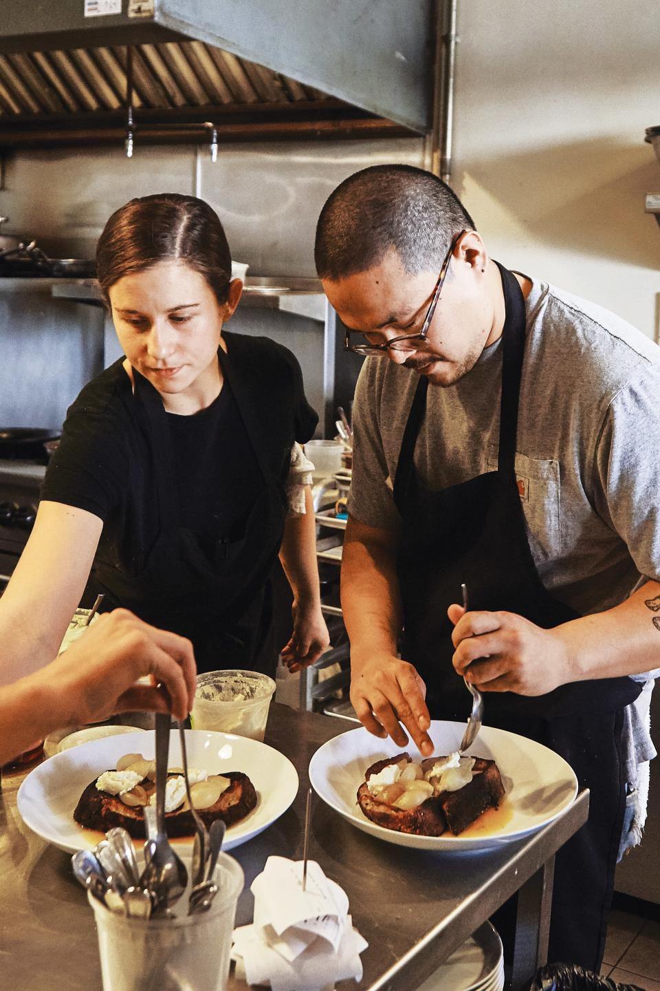 Line cook Hailee Catalano and lead line cook Chuck Cruz plating in the kitchen.