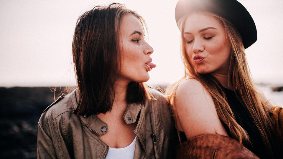 Two teenage girls having fun on beach pulling faces.