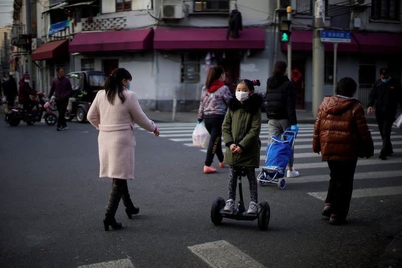 Una niña con una máscara en patinete por una calle del centro de Shangái, China