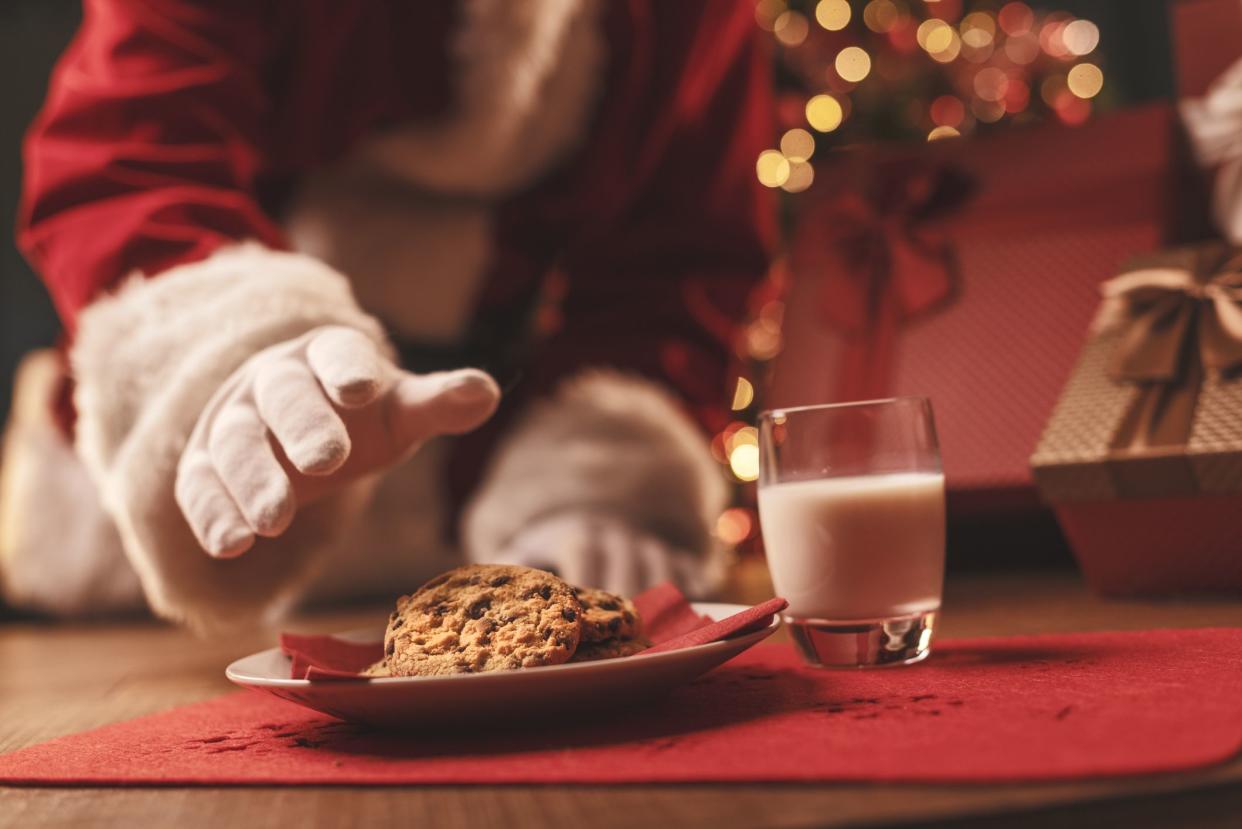 Santa Claus having a delicious snack, he is eating cookies and drinking milk, Christmas and holidays concept