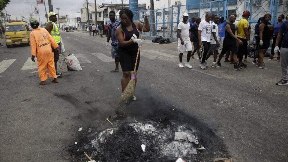 Volunteers sweep burned out tires on the roads in Lagos Saturday, Oct. 24, 2020. (AP Photo/Sunday Alamba)