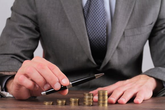 Person using a pen to highlight progressively larger stacks of coins,