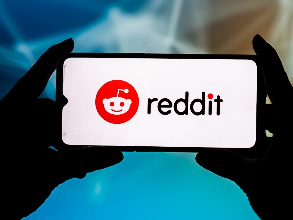 Illustration of Reddit logo on white screen with hands holding phone