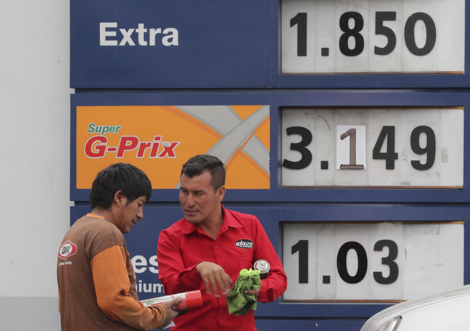 An attendant shows an automotive product to a driver in front of a display with new fuel prices at a gas station in Quito, Ecuador, Tuesday, Oct. 15, 2019. The recent strike that paralyzed the Andean nation for almost two weeks, has left a gaping hole in Ecuador’s economy, this after President Lenin Moreno called back his elimination of fuel subsidies which provoked the violent protests. (AP Photo/Dolores Ochoa)