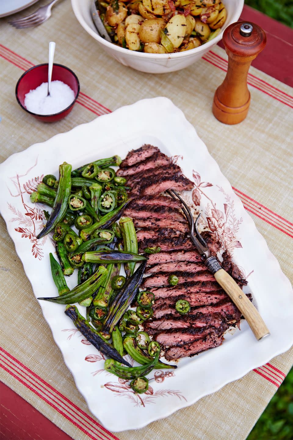 coffee and brown sugar crusted skirt steak sliced on a rectangle serving plate with grilled okra and jalapeños
