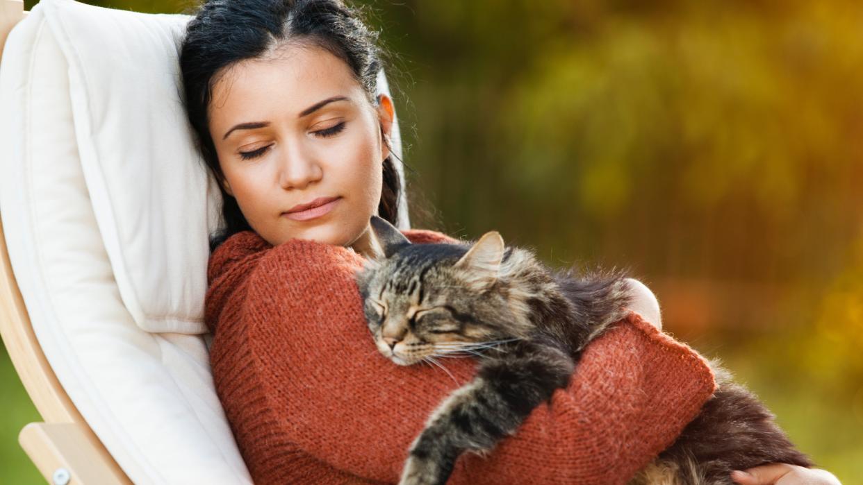  Woman with eyes closed sitting in chair outside with sleeping cat in her arms. 